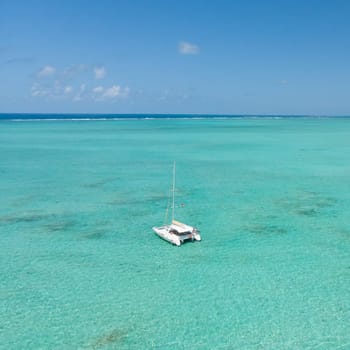 Catamaran sailing boat in turquoise sea lagoon on tropial Mauritius island. Aerial, top down drone view.