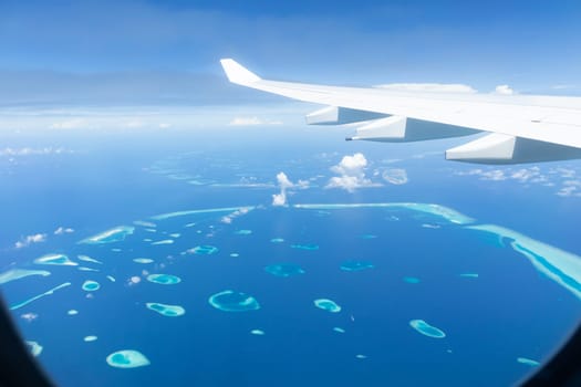 Top view of Maldive islands from airplane window with airplane's wing.