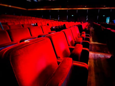 a row of empty red velvet armchairs inside an auditorium. Interior of a theater or cinema