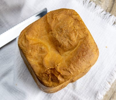 Fresh homemade bread stands on a white towel on a wooden board, next to a knife for cutting bread. Top views.
