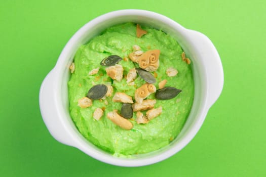 Two curd desserts: one with blueberries and nuts and the other with avocado and kiwi, next to there are pumpkin seeds and nuts.