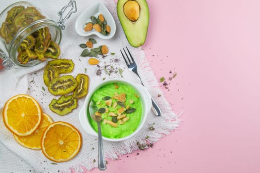 Two curd desserts: one with blueberries and nuts and the other with avocado and kiwi, next to there are pumpkin seeds and nuts.