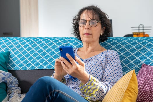 cheerful brunette senior woman using a smartphone while sitting on sofa