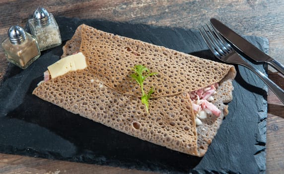Breton crepe with cheese and bacon on a black slate