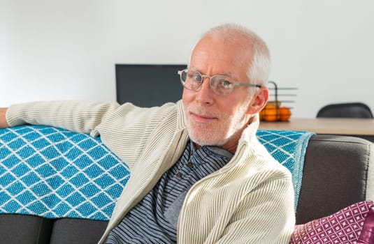Senior with white hairs wearing eyeglasses sitting on a sofa
