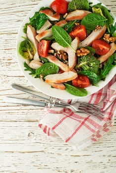 Healthy green salad with chicken breast tomato and nuts on wooden table