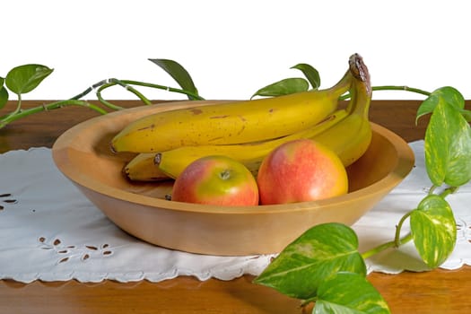 Hand-turned wooden bowl with bananas and apple stands on a table against white background