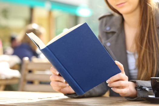 Close up of young woman hands reading a hard cover blue book on a cafe terrace