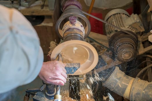 Making a wooden bowl on a lathe in an old small workshop with flying wooden shavings