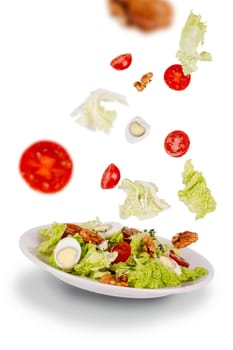 Salad of fresh green leaves, cherry tomatoes, quail eggs, walnuts on a flying saucer with flying ingredients