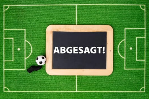 Concept photo: soccer field with chalkboard says in german language "abgesagt"" means canceled"