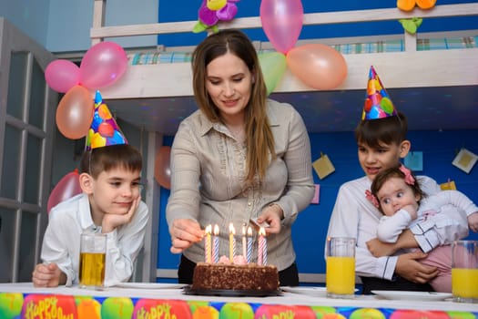 Mom lights candles at a birthday celebration in the children's room, around the children