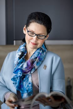 Middle-aged brunette woman reading a magazine with interest.