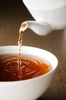 Teapot pouring fresh hot tea in to Cup, on dark background. The Time of Tea Break.
