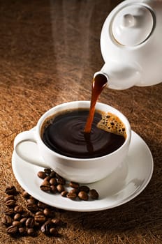 Coffee pot pouring fresh hot coffee into cup on dark background