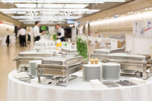 Waiters prepare buffet before a coffee break at business conference meeting. Focus on plates and dishes on the table.