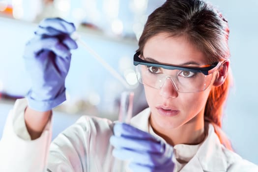 Life scientists researching in laboratory. Focused female life science professional pipetting solution into the glass cuvette. Lens focus on researcher's eyes. Healthcare and biotechnology concept.