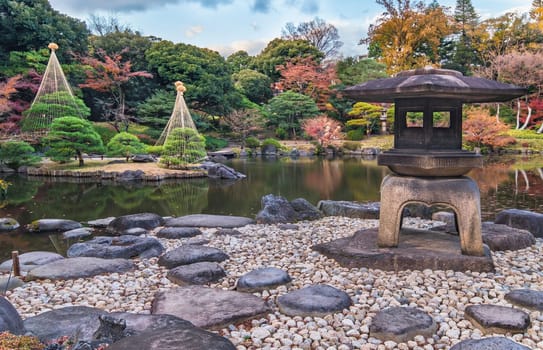 Tokyo Metropolitan Park KyuFurukawa's japanese garden's Yukimi stone lantern overlooking by red maple momiji leaves in autumn.
