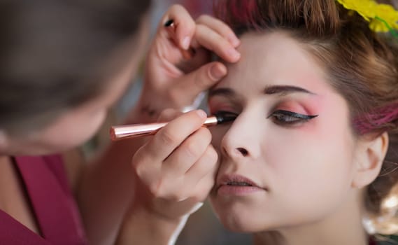 Portrait of a beautiful woman in beauty salon. Makeup artist applies eyeliner on a face