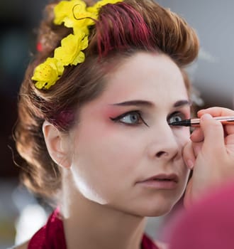 Portrait of a beautiful woman in beauty salon. Makeup artist applies eyeliner on a face