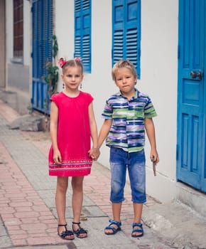 Kids walking by the street next to shutter blue window