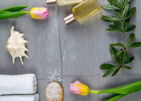 Two towels, body care oil, tulips, green branch and sea salt stand on a concrete background. Spa treatments concept, healthy body.