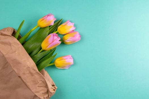 Bouquet of yellow tulip flowers in brown paper bag on mint background.