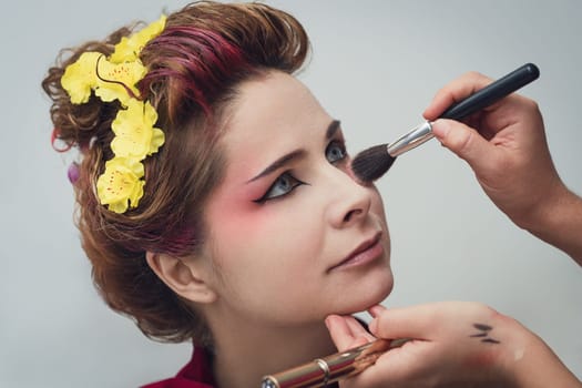 Portrait of a beautiful woman in beauty salon. Makeup artist applies powder on a face