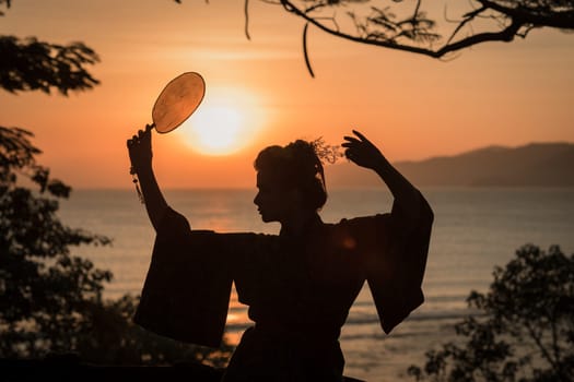 Silhouette of Japanese Geisha in kimono with fan at sunrise