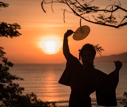 Silhouette of Japanese Geisha in kimono with fan at sunrise