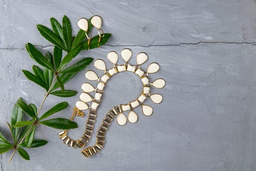 Jewelry, pendant around the neck along with a green branch laid on a concrete background. To the right of the composition is free space.