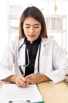 Confident female doctor medical professional sitting in examination room in hospital clinic sign document. No face crop