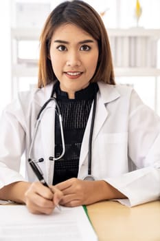 Confident female doctor medical professional sitting in examination room in hospital clinic sign document. No face crop