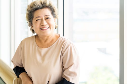 Portrait of happy and smile elderly senior adult female standing beside window in domestic living room - recovery and rehabilitation concept
