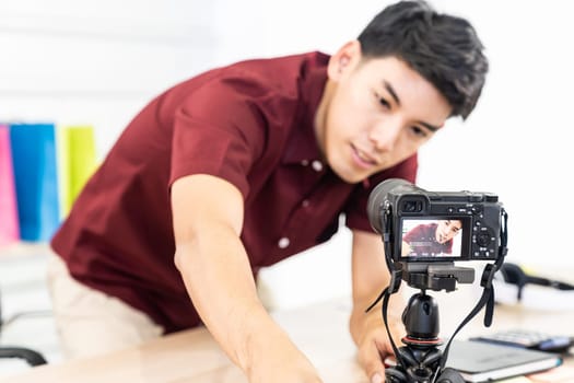 Young asian male blogger setting up camera for recording live vlog video tutorial session at home. IT blogging or vlogging, social media hobby broadcasting, or online learning course concept.
