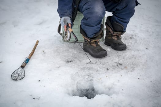 Baikal lake, Siberia, Russia - March 05, 2020 : Winter ice fishing. A fisherman is fishing on spinings near tents and cars on Lake Baikal on a March day. Baikal lake, Siberia, Russia
