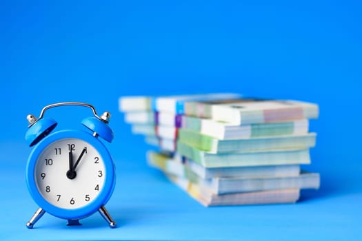 In the foreground is an alarm clock, in the background is a stack of bills