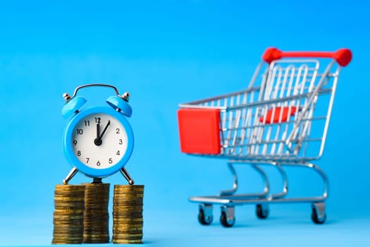 A clock stands on a stack of coins, in the background a grocery cart