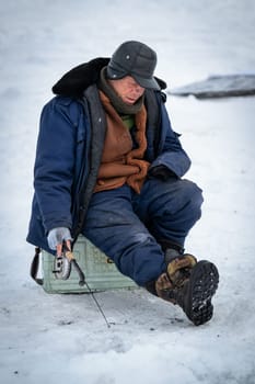 Baikal lake, Siberia, Russia - March 05, 2020 : Winter ice fishing. A fisherman is fishing on spinings near tents and cars on Lake Baikal on a March day. Baikal lake, Siberia, Russia