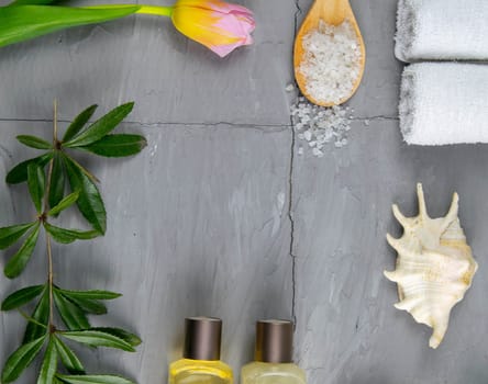 Two towels, body care oil, tulips, green branch and sea salt stand on a concrete background. Spa treatments concept, healthy body.