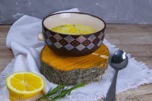 Potato cream soup with mushrooms, carrots and cheese. Top view. Soup in a brown plate, stands on a wooden stand, next to a hour, spoon, spices and lemon.