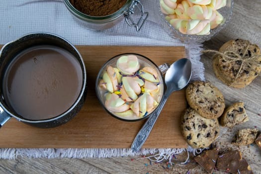 Cocoa with marshmallows and chocolate oven and slices of chocolate stands on a wooden table.