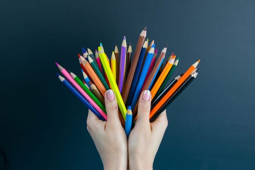 bunch of colored pencils in hand. A woman's hand holds a set of colored pencils on a black background.