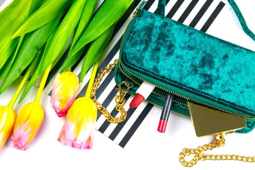Tulips with green women's clutch and women's cosmetics on a white background.