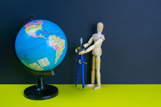 Wooden man figurine with compass and globe on the yellow table.