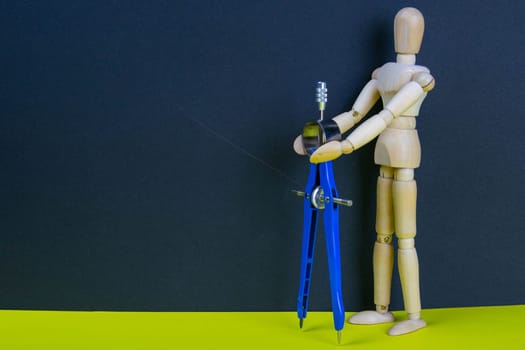 Wooden man figurine with compass on the yellow table.