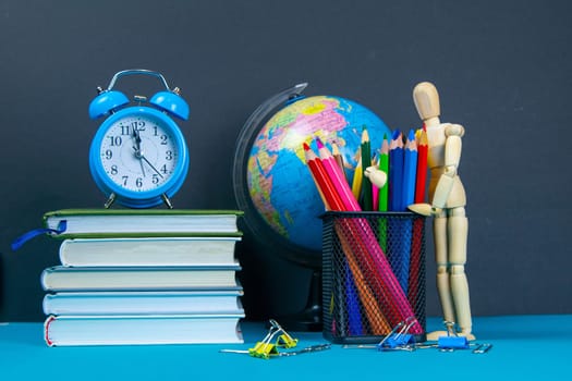 The globe and the clock stand on a stack of books, next to a glass of pencils and the pyramid is folded with wooden cubes and the figure of a wooden man hugs pencils.