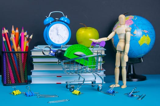 The globe and the clock stand on a stack of books, next to a glass of pencils and the pyramid is folded with wooden cubes and the figure of a wooden man pushes a trolley filled with clerical courtesy.