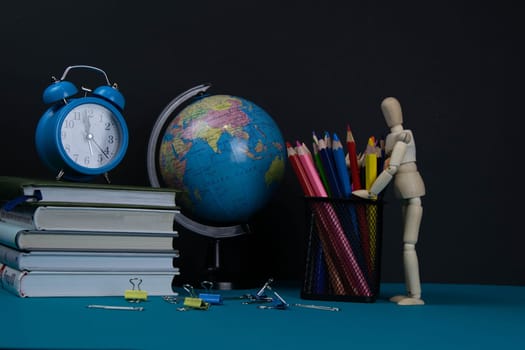 The globe and the clock stand on a stack of books, next to a glass of pencils and the pyramid is folded with wooden cubes and the figure of a wooden man hugs pencils.