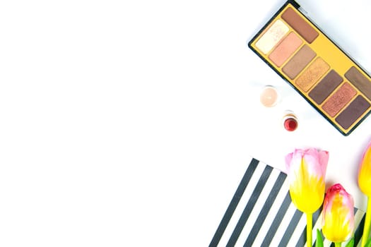 Tulips with green women's clutch, pallet with shadows and women's cosmetics on a white background.